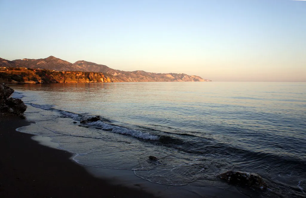 A Nerja beach below the town cliffs, busy with summer visitors who fill the central car parks by late morning