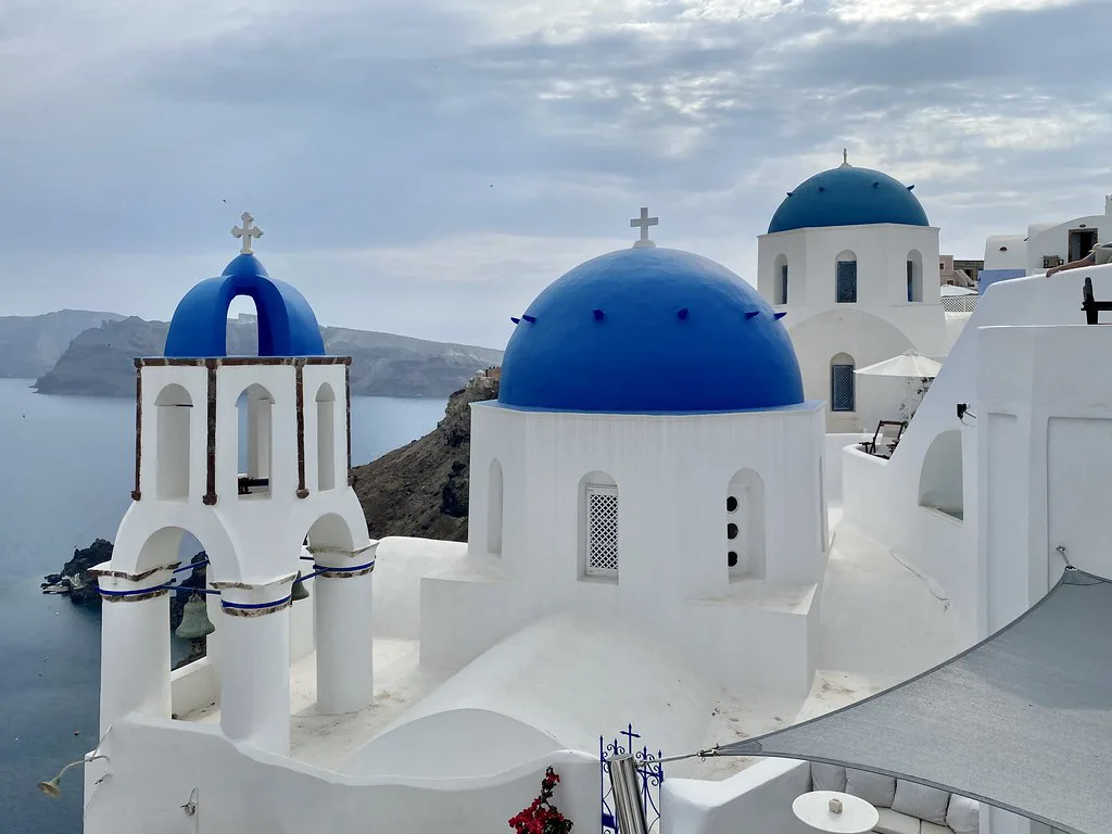 The blue-domed churches of Oia perched on the Santorini caldera edge, a short walk from the village's free parking lots