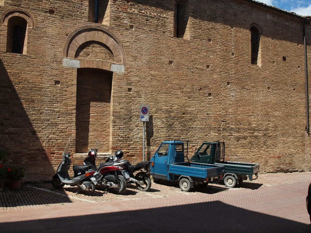 A car parking area near San Gimignano with vehicles lined up below the Tuscan hill town